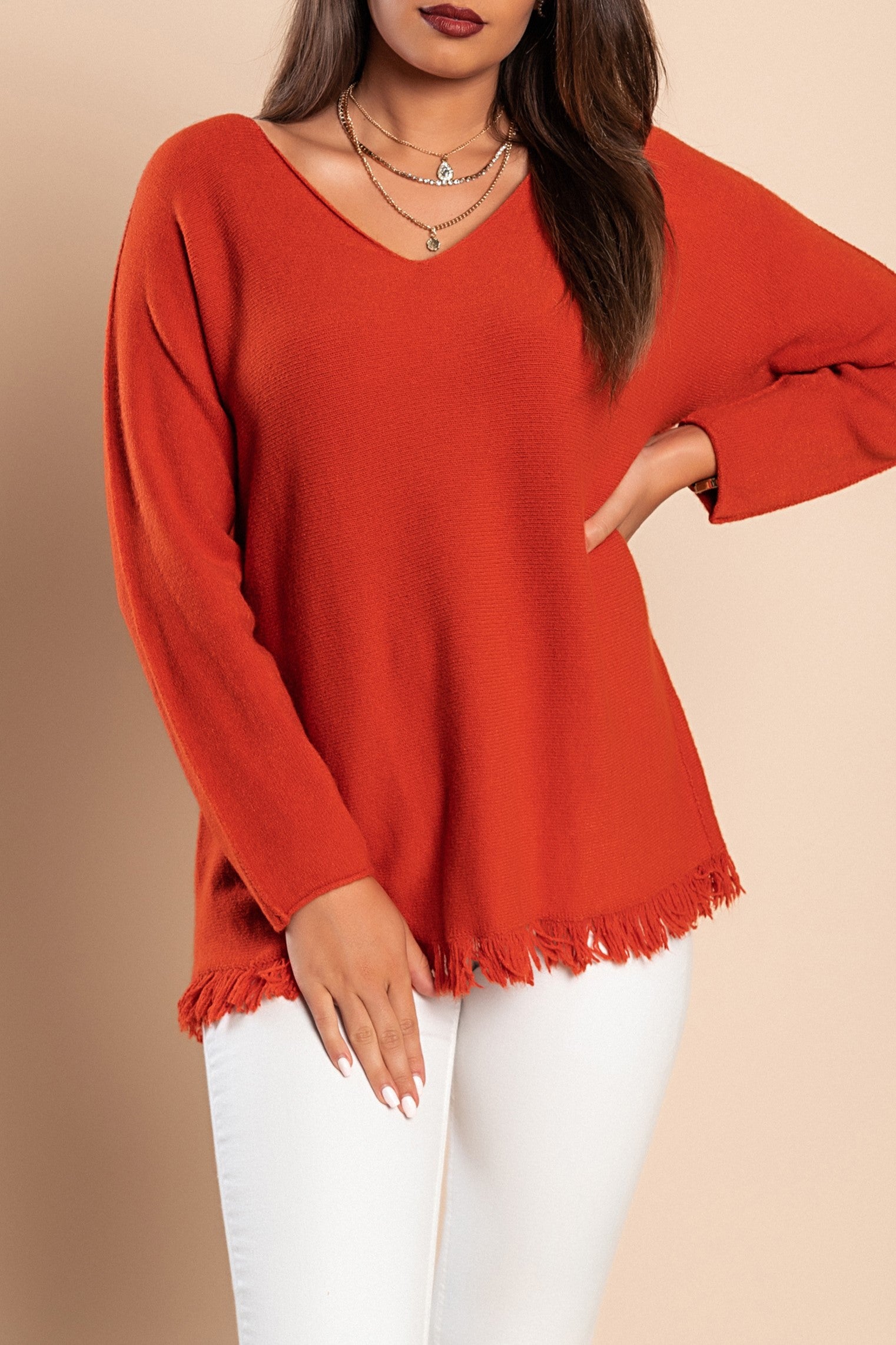 Brick colored sweater with tassels at the bottom, featuring a V-neckline and long sleeves, made from soft knitwear.