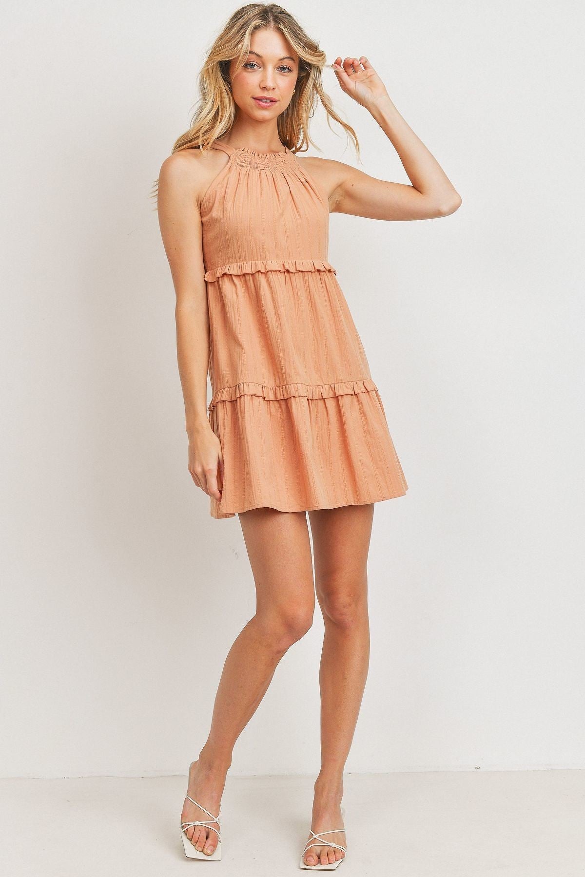 A stylish blush tiered dress made from textured woven fabric, featuring a halter neck and ruffled layers, perfect for summer occasions.