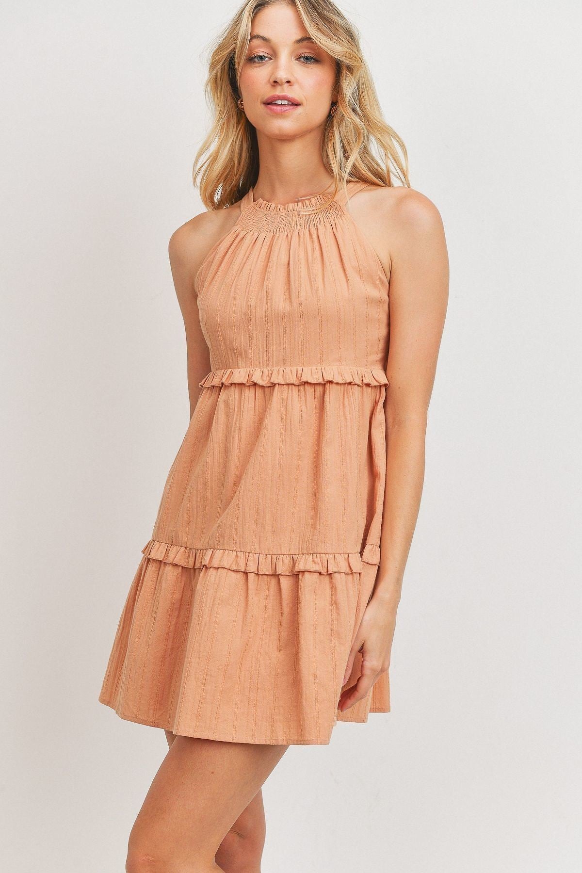 A stylish blush tiered dress made from textured woven fabric, featuring a halter neck and ruffled layers, perfect for summer occasions.