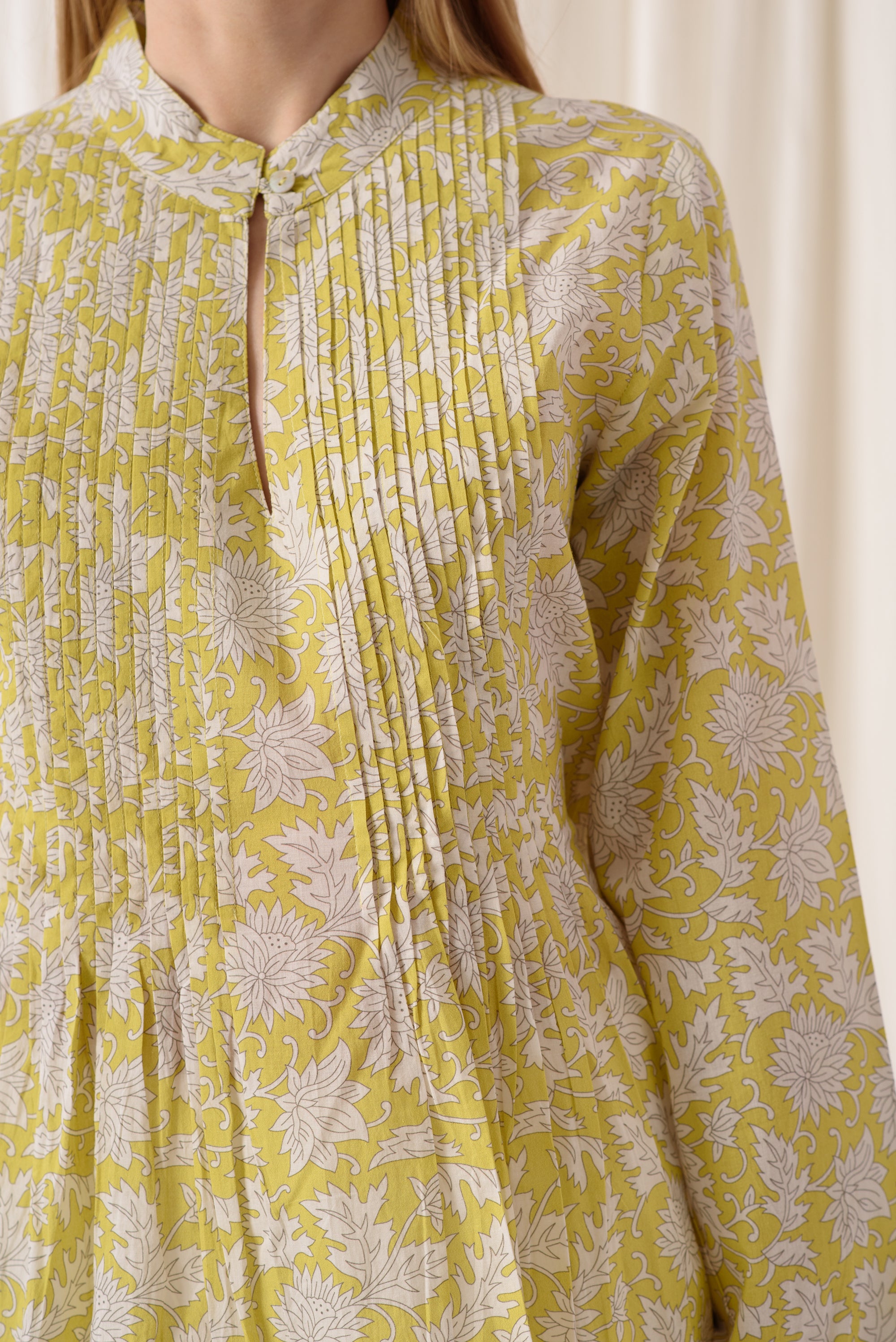 A stylish pleated top in sunny yellow with a crew neck and upside button front, showcasing its chic design and comfortable fabric.