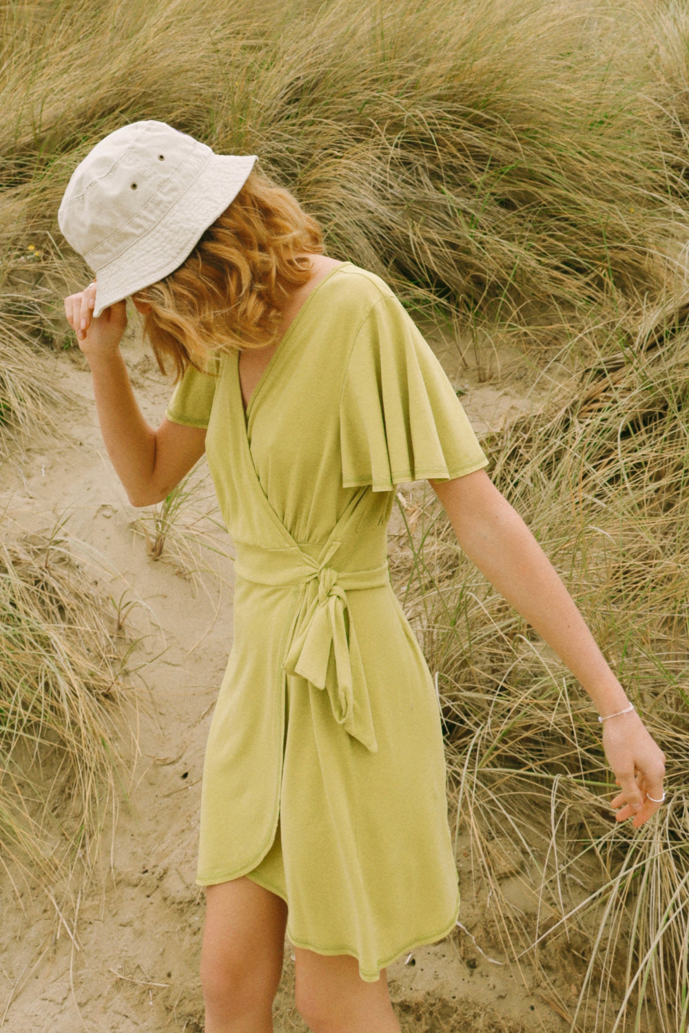 A stylish woman wearing a yellow wrap dress with flouncy sleeves, showcasing a feminine silhouette and vintage-inspired design.