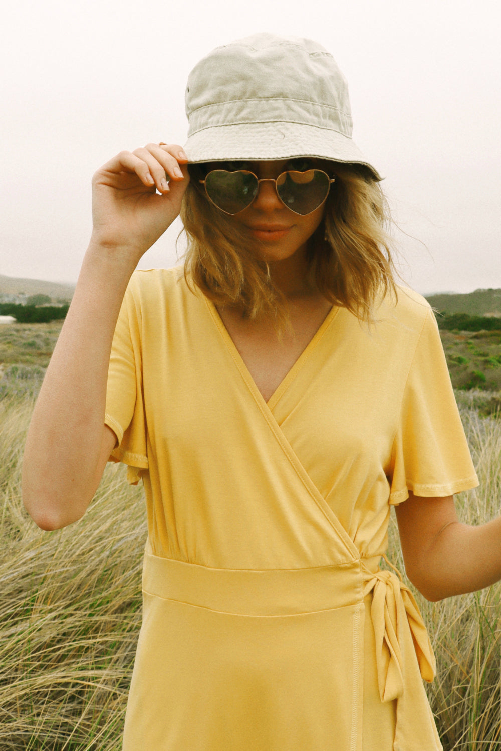 A stylish woman wearing a yellow wrap dress with flouncy sleeves, showcasing a feminine silhouette and vintage-inspired design.