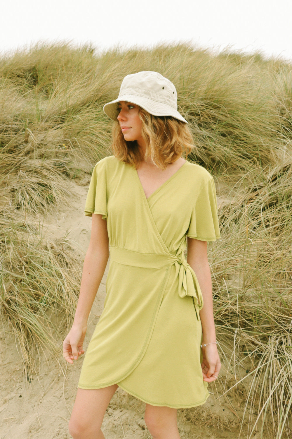 A stylish woman wearing a yellow wrap dress with flouncy sleeves, showcasing a feminine silhouette and vintage-inspired design.