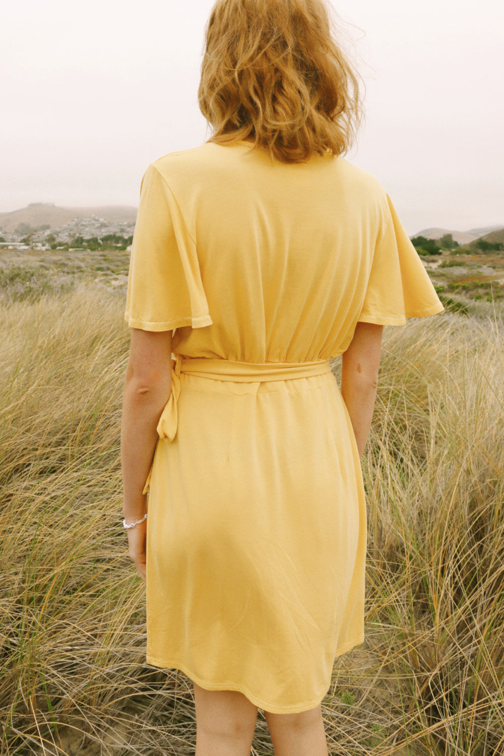 A stylish woman wearing a yellow wrap dress with flouncy sleeves, showcasing a feminine silhouette and vintage-inspired design.