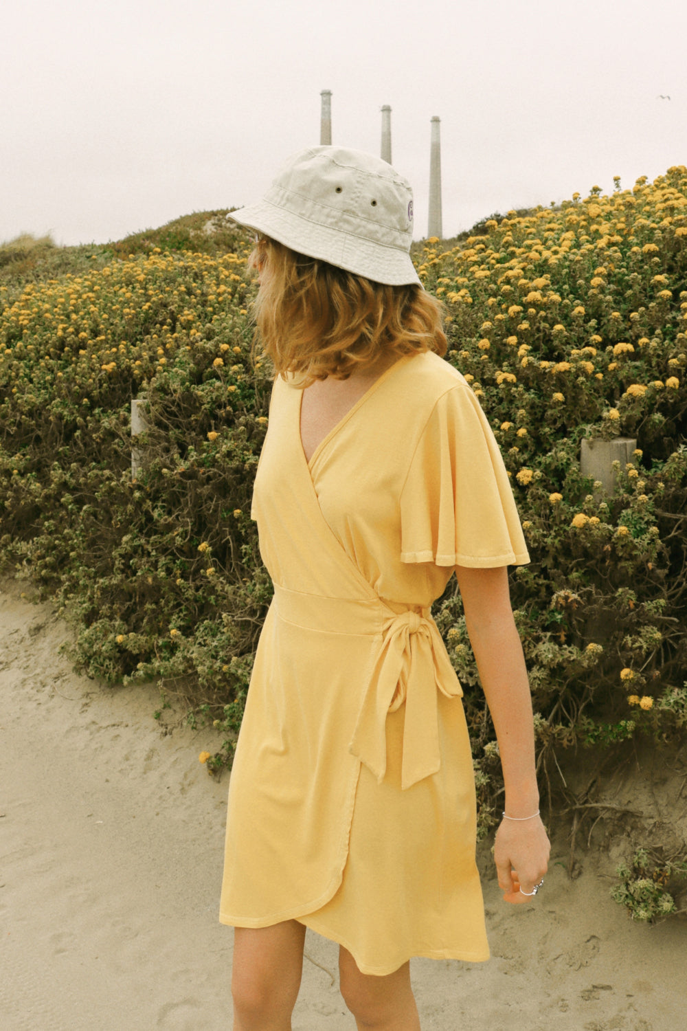 A stylish woman wearing a yellow wrap dress with flouncy sleeves, showcasing a feminine silhouette and vintage-inspired design.