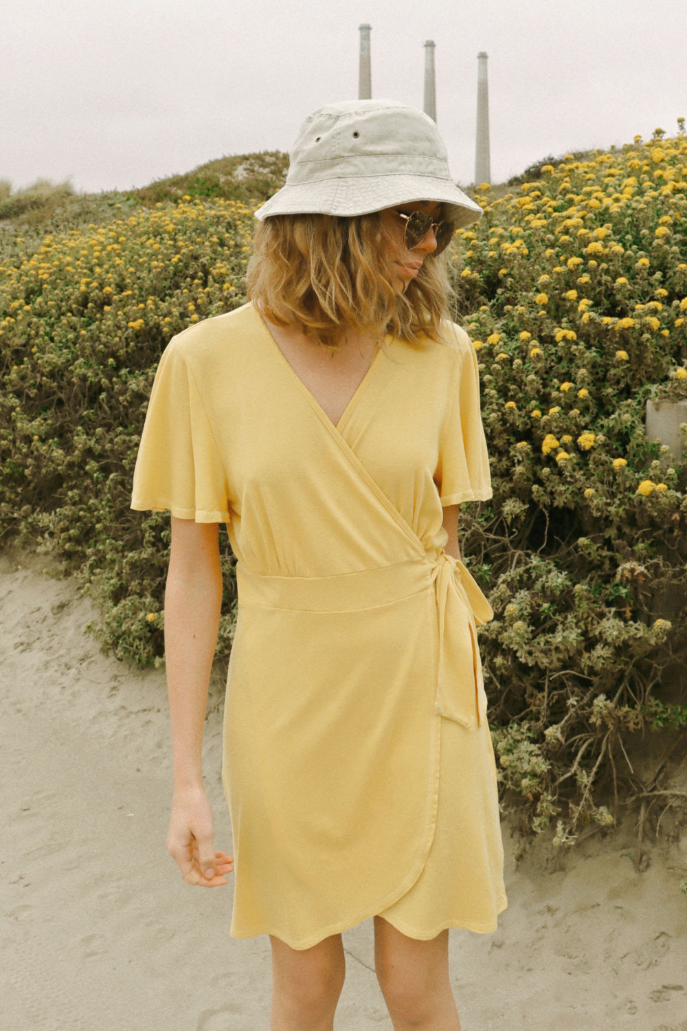 A stylish woman wearing a yellow wrap dress with flouncy sleeves, showcasing a feminine silhouette and vintage-inspired design.