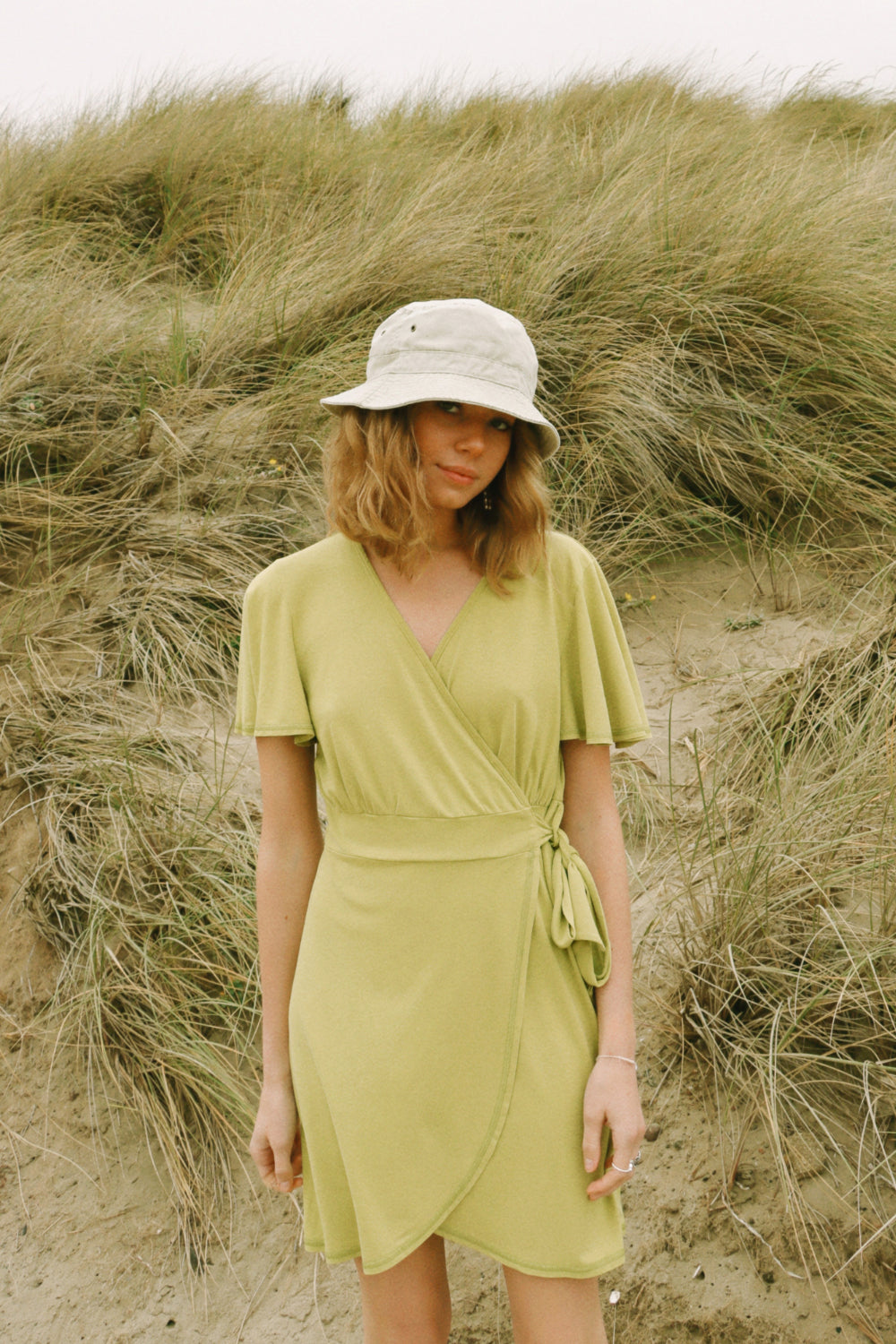 A stylish woman wearing a yellow wrap dress with flouncy sleeves, showcasing a feminine silhouette and vintage-inspired design.