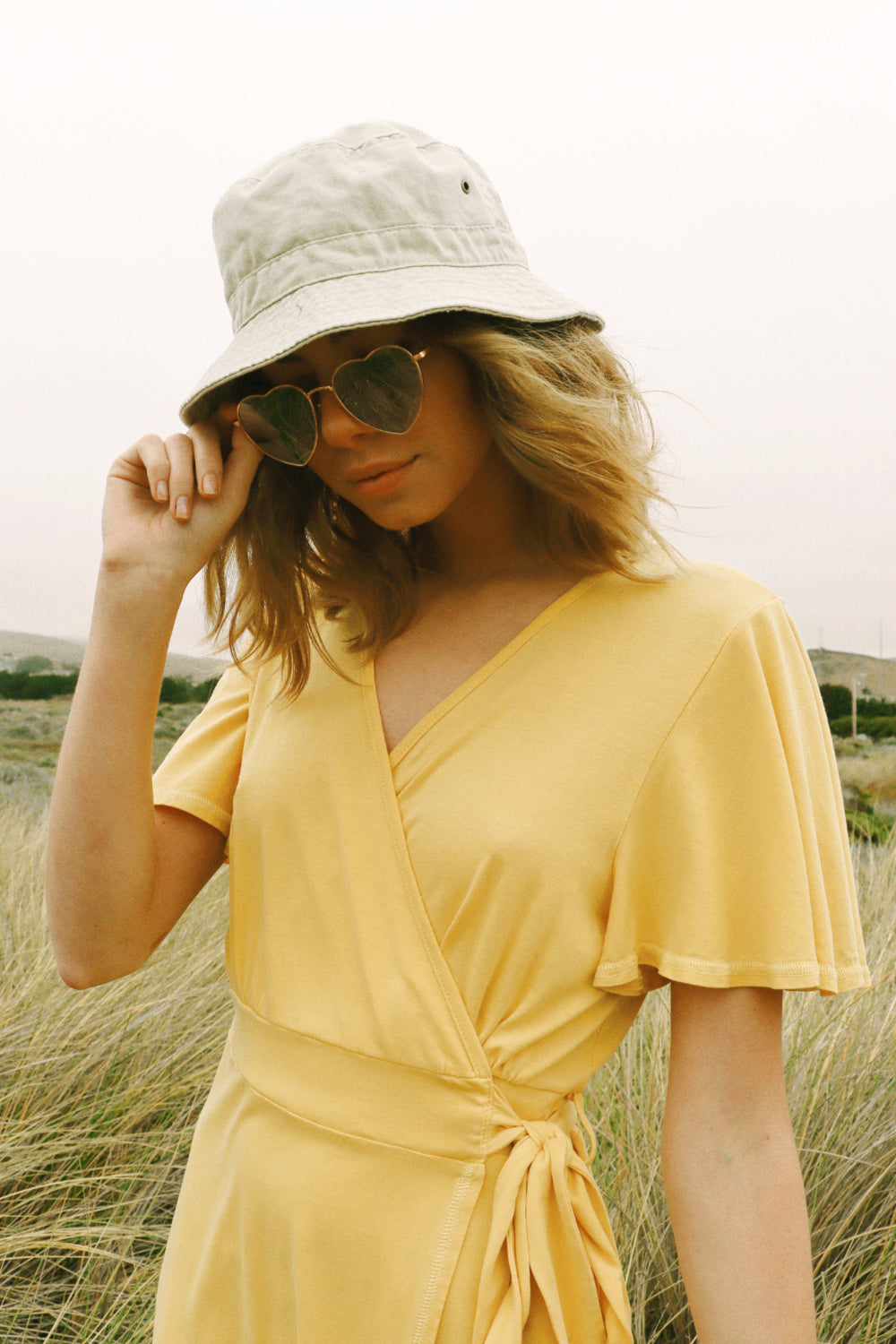 A stylish woman wearing a yellow wrap dress with flouncy sleeves, showcasing a feminine silhouette and vintage-inspired design.