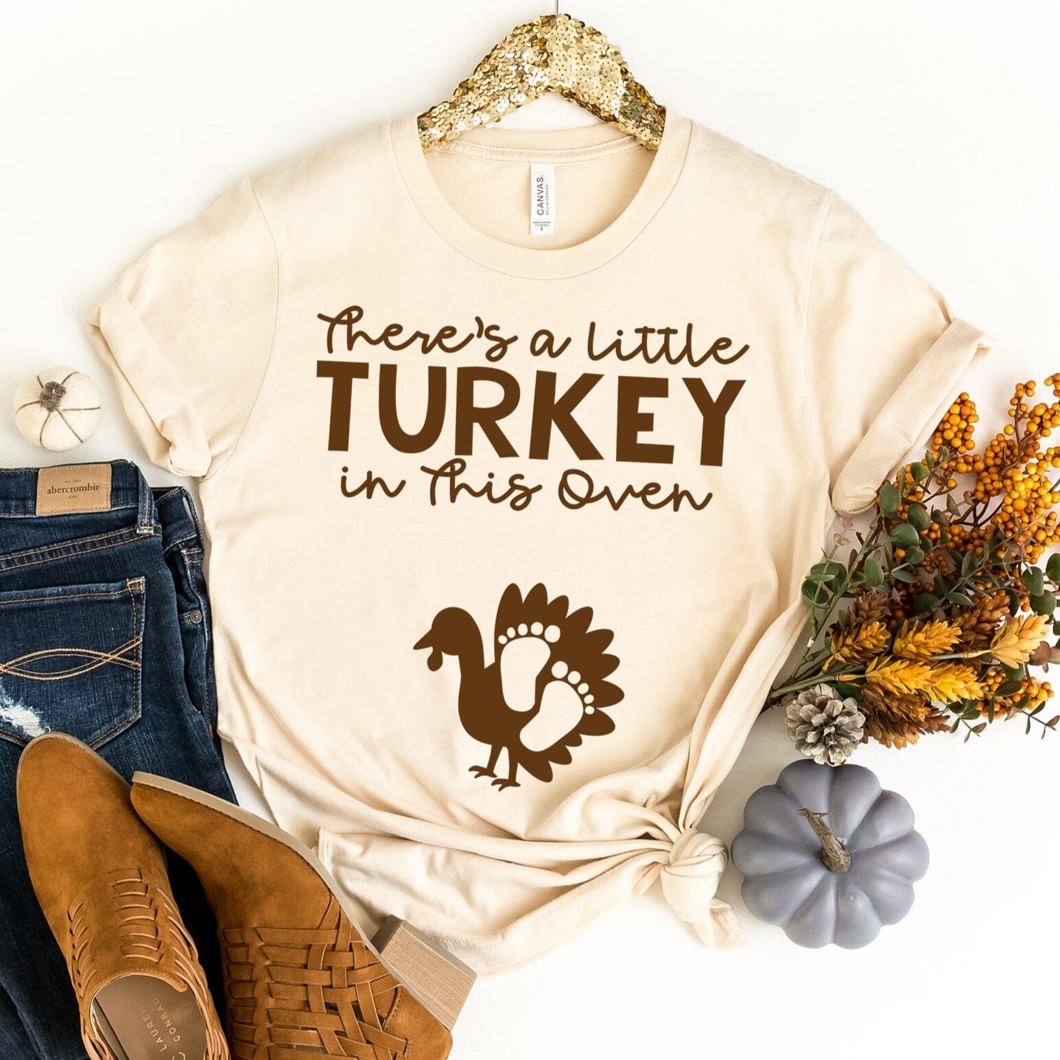 A comfortable unisex T-shirt featuring a playful Thanksgiving graphic that reads 'There's a Little Turkey in This Oven'.