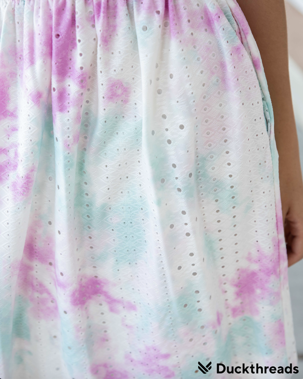 A vibrant Tie Dye Eyelet Dress in Teal and Pink, featuring an elastic waistband and pockets, perfect for summer outings.