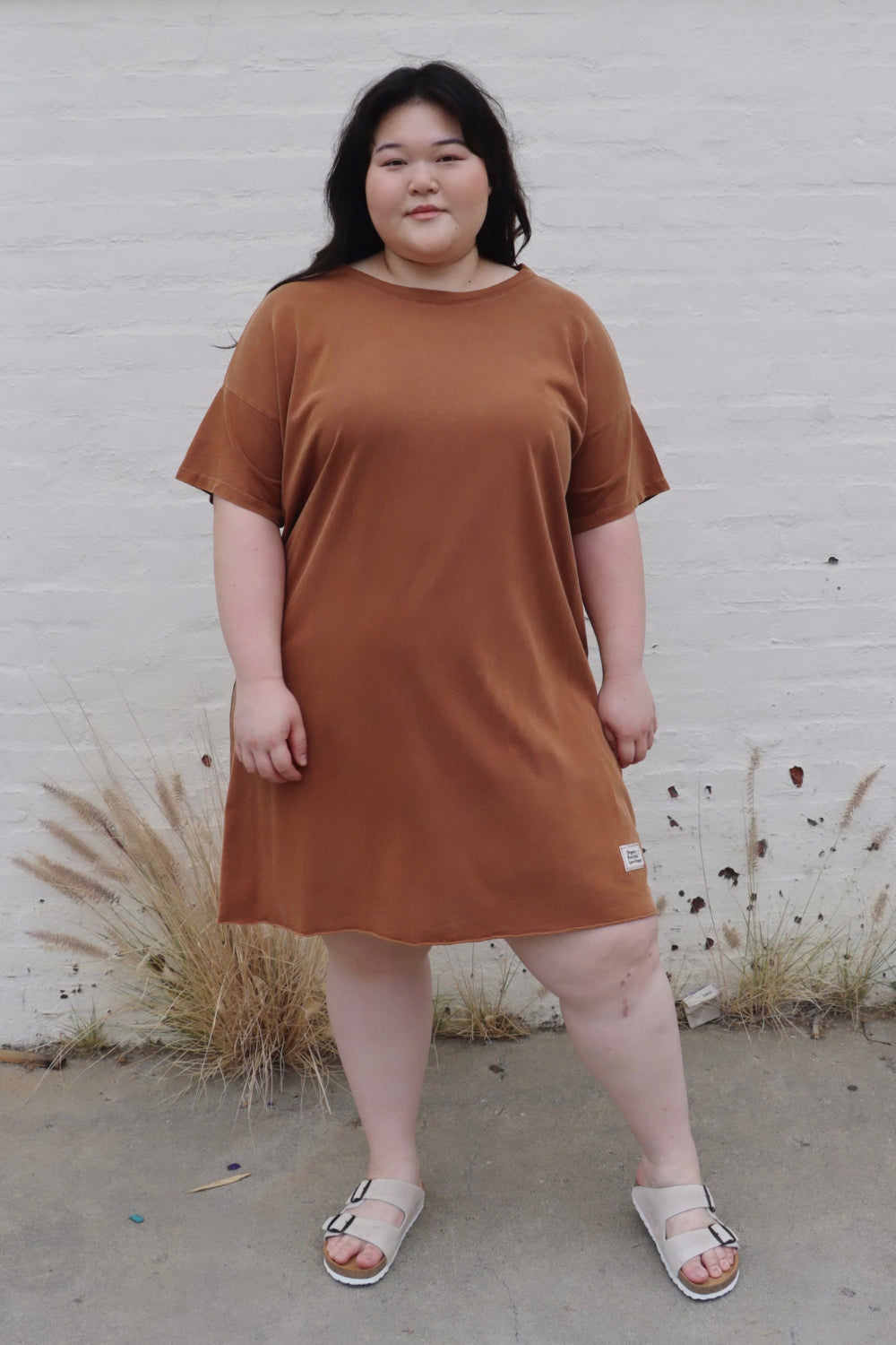 A relaxed fit Topanga Dress in saddle color, made from 100% organic cotton, displayed on a mannequin with sandals and a tote.