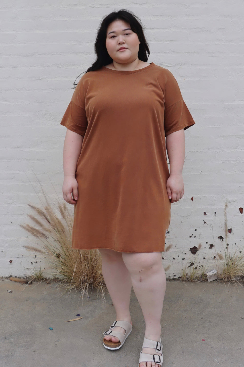 A relaxed fit Topanga Dress in saddle color, made from 100% organic cotton, displayed on a mannequin with sandals and a tote.