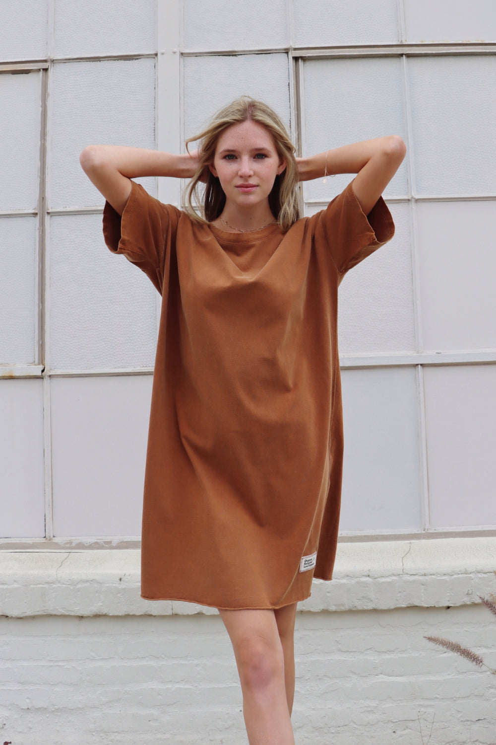 A relaxed fit Topanga Dress in saddle color, made from 100% organic cotton, displayed on a mannequin with sandals and a tote.