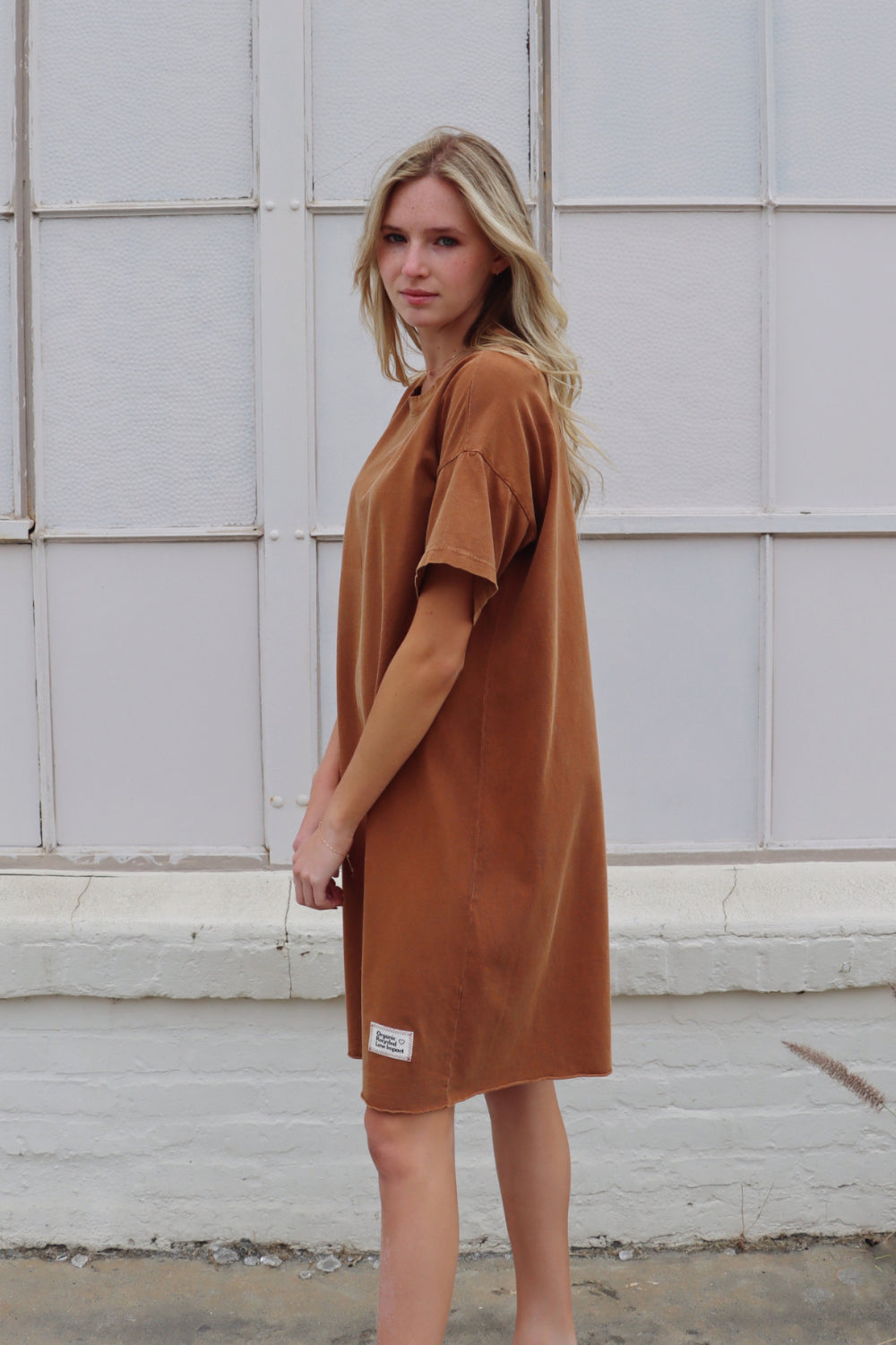 A relaxed fit Topanga Dress in saddle color, made from 100% organic cotton, displayed on a mannequin with sandals and a tote.