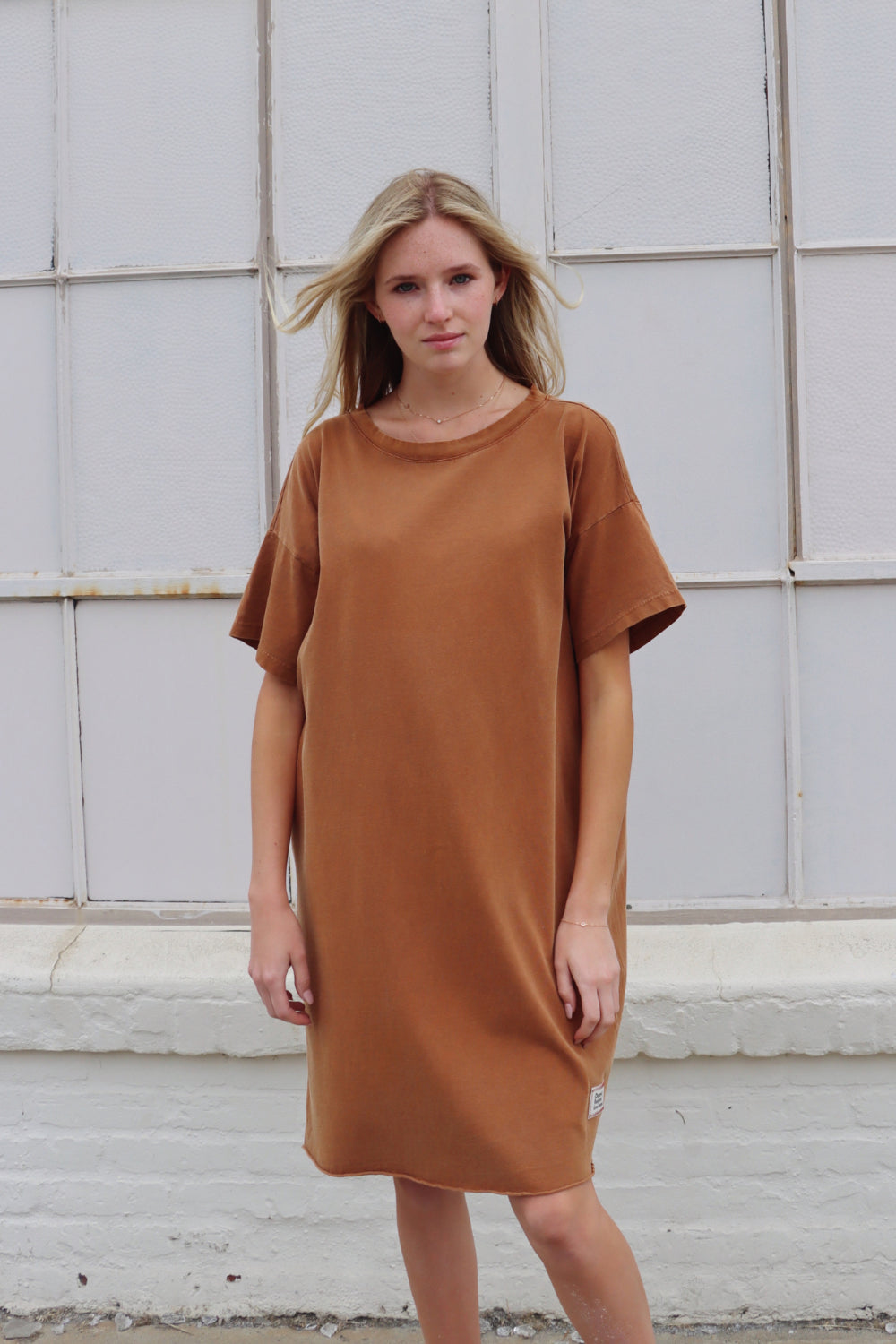 A relaxed fit Topanga Dress in saddle color, made from 100% organic cotton, displayed on a mannequin with sandals and a tote.