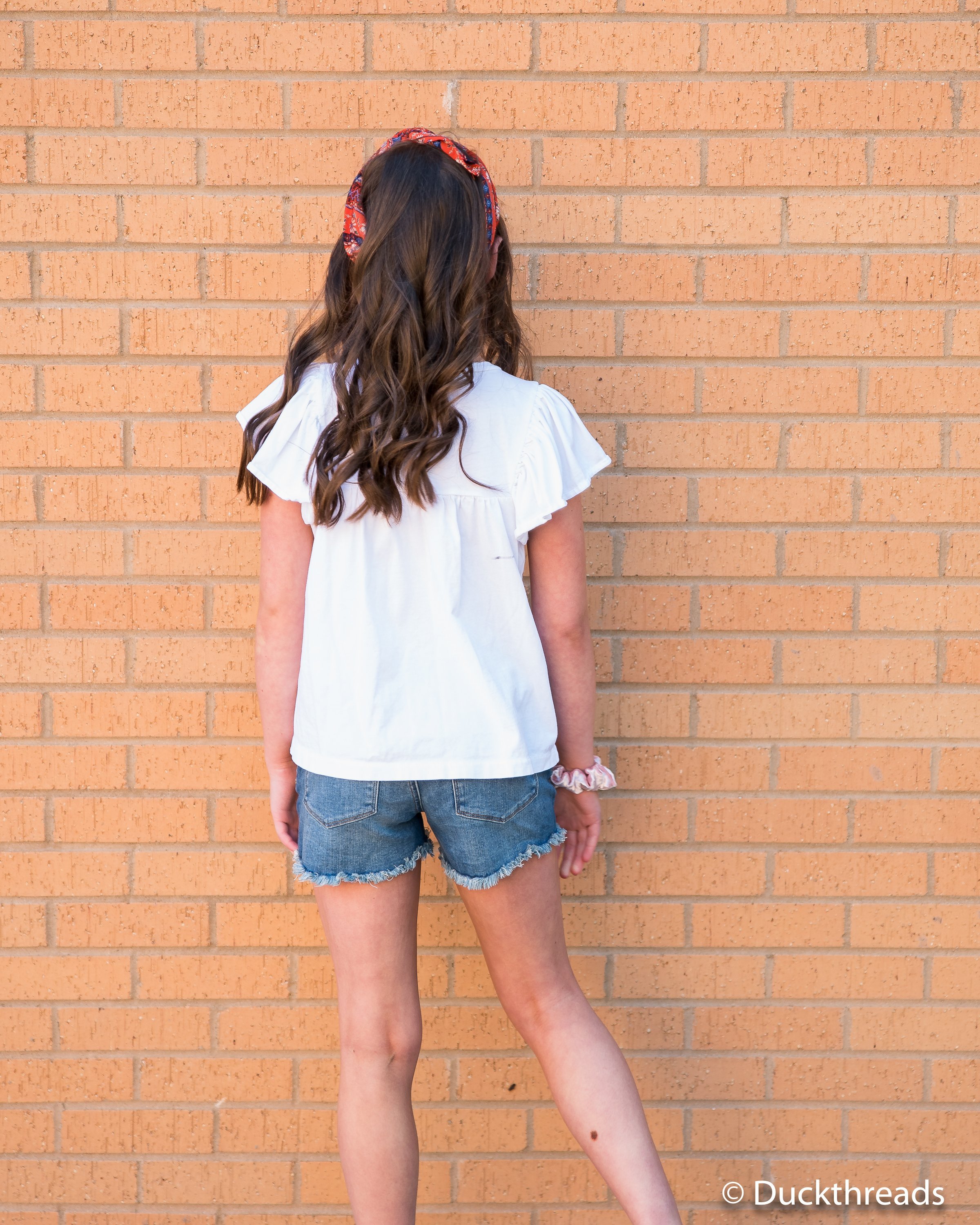 Tractr Dark Distressed Denim Shorts for Girls featuring a frayed hem and five pockets, styled with a casual tee.