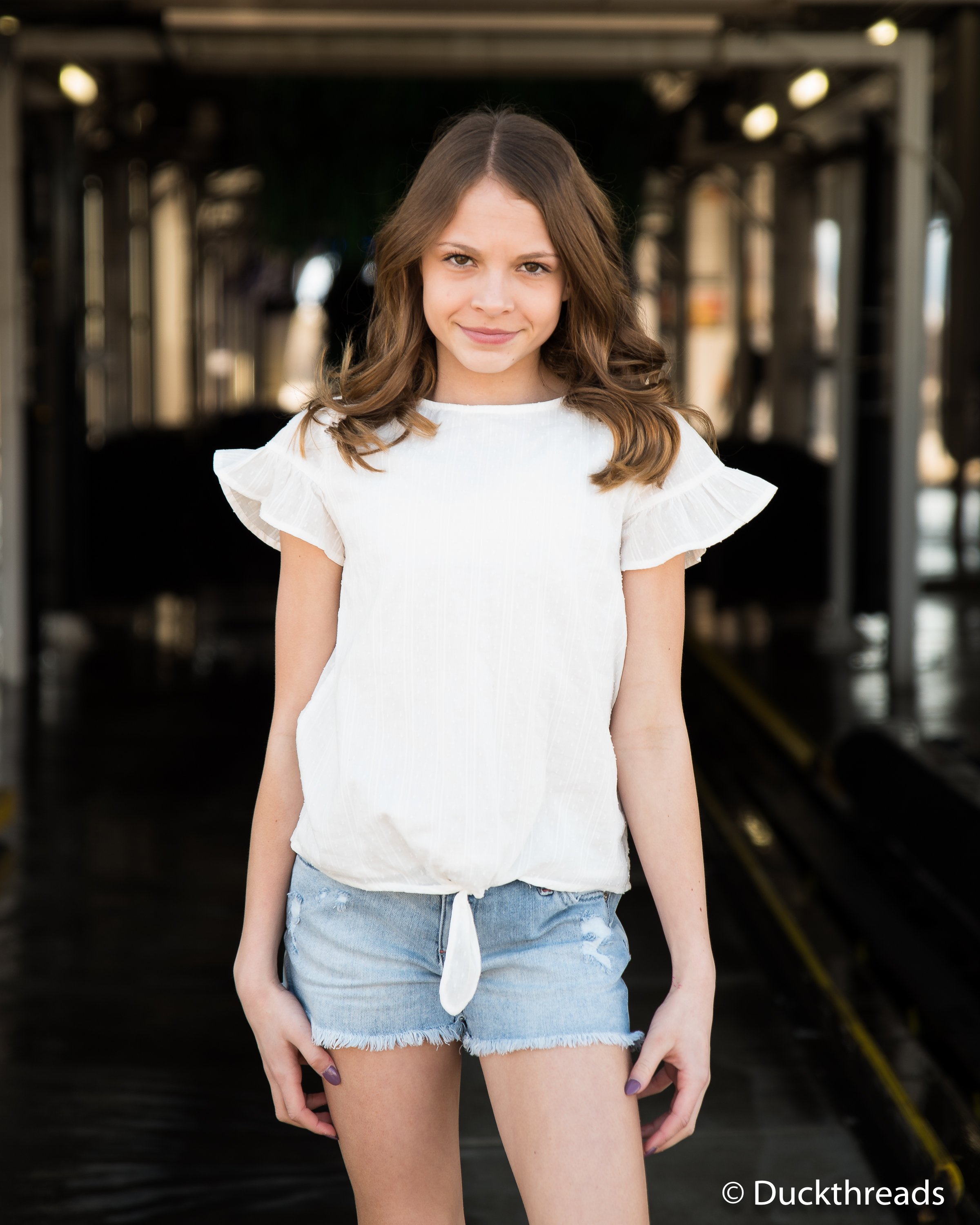 Tractr Stars & Stripes Denim Shorts for Girls featuring a pale indigo color, distressed front, and a patriotic stars and stripes pattern on the back.