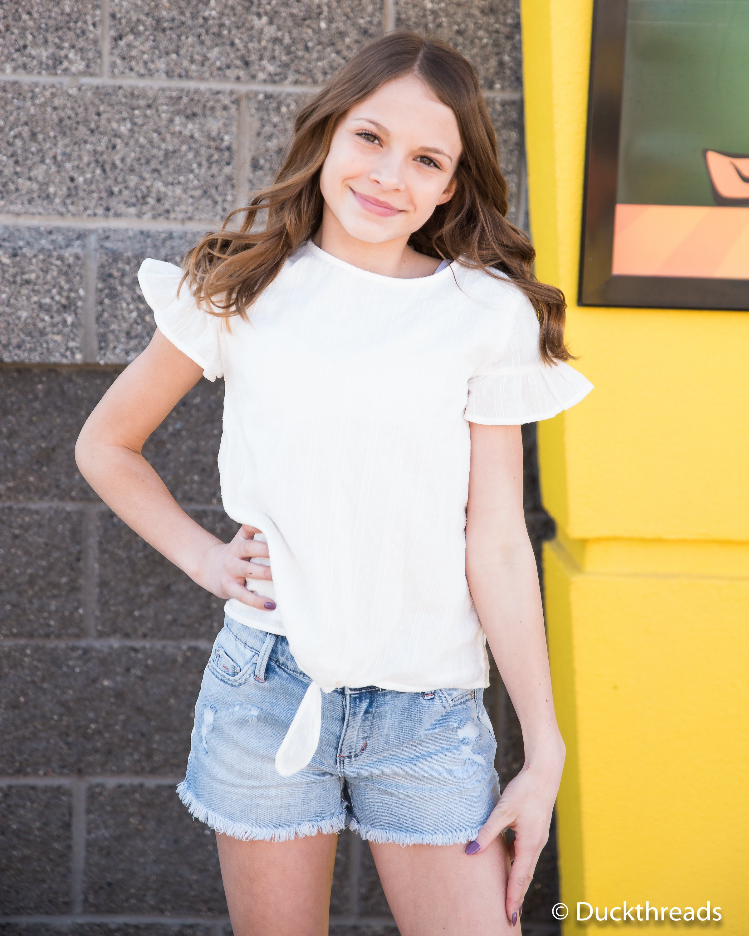 Tractr Stars & Stripes Denim Shorts for Girls featuring a pale indigo color, distressed front, and a patriotic stars and stripes pattern on the back.