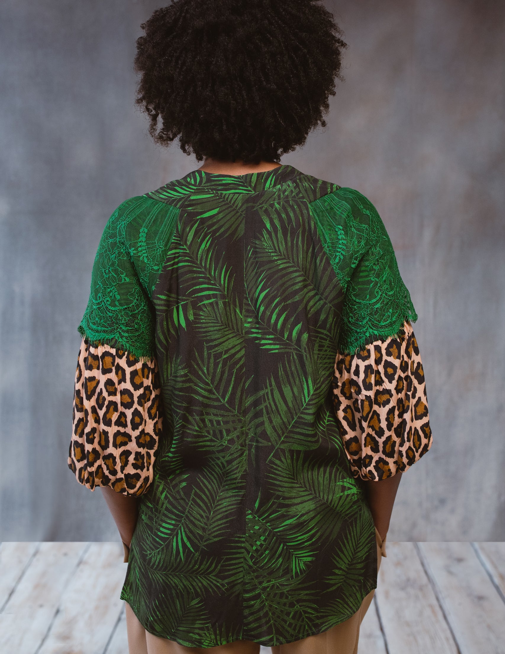 A stylish Tropical Print Top featuring a subtle tropical design, lace accents, and statement sleeves, perfect for various occasions.