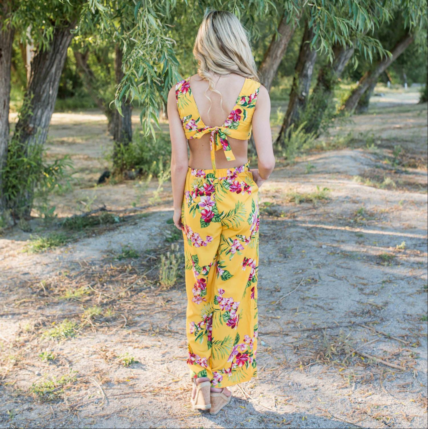 A stylish Tropical Tie Back Jumpsuit featuring a vibrant floral pattern, deep V back, and wide leg design, perfect for summer outings.