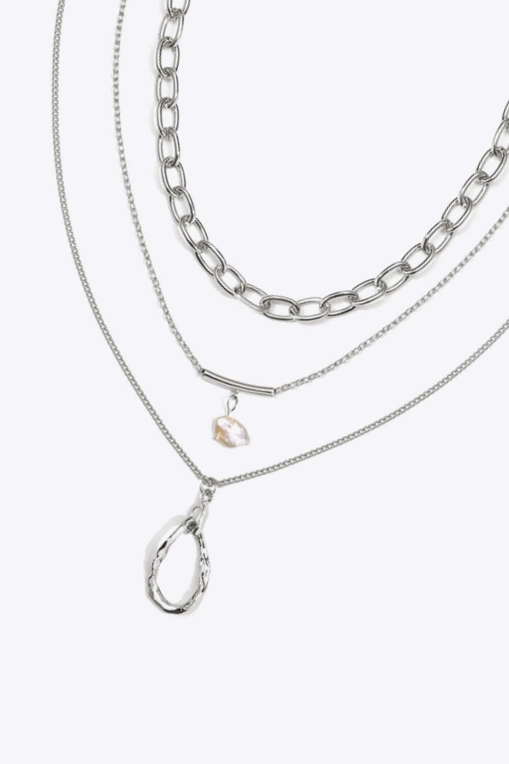 A stylish triple-layered necklace featuring stainless steel, 18k gold plating, and a freshwater pearl, displayed in a studio setting.