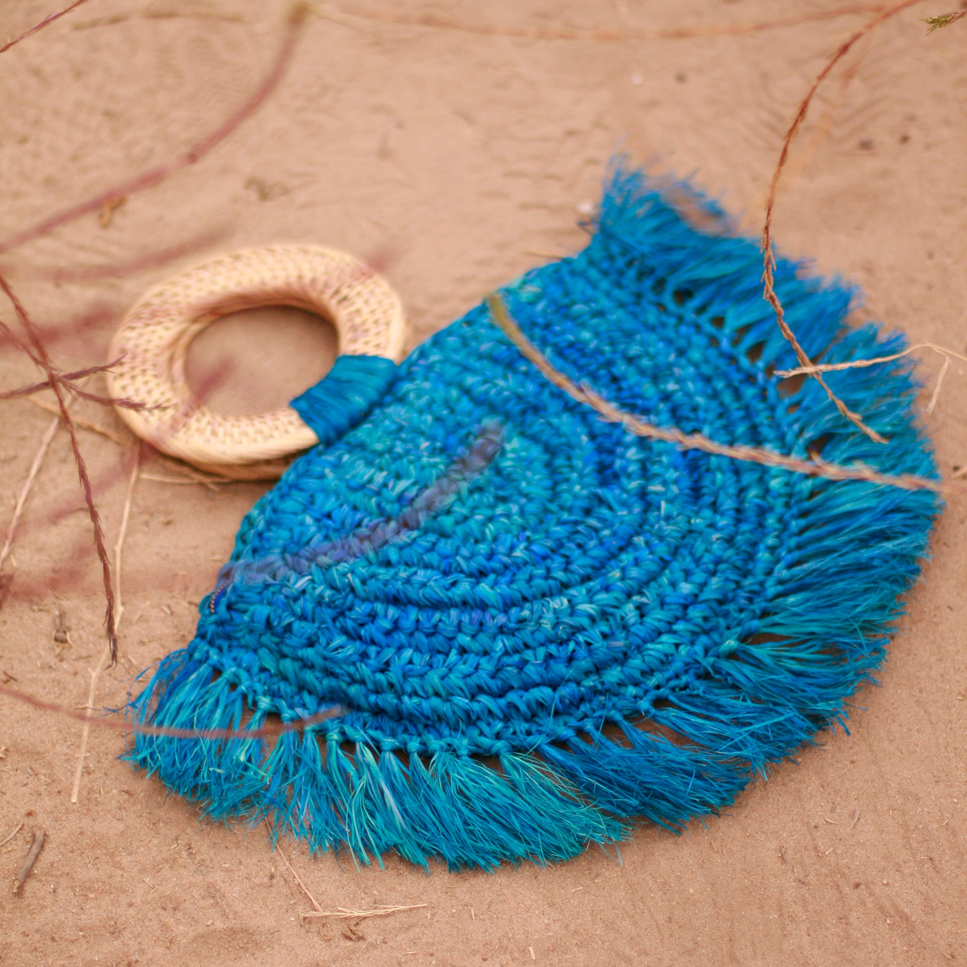 Warrior Raffia Straw Bag in Blue, handcrafted with natural Raffia straw, featuring fringes and a stylish rattan handle.