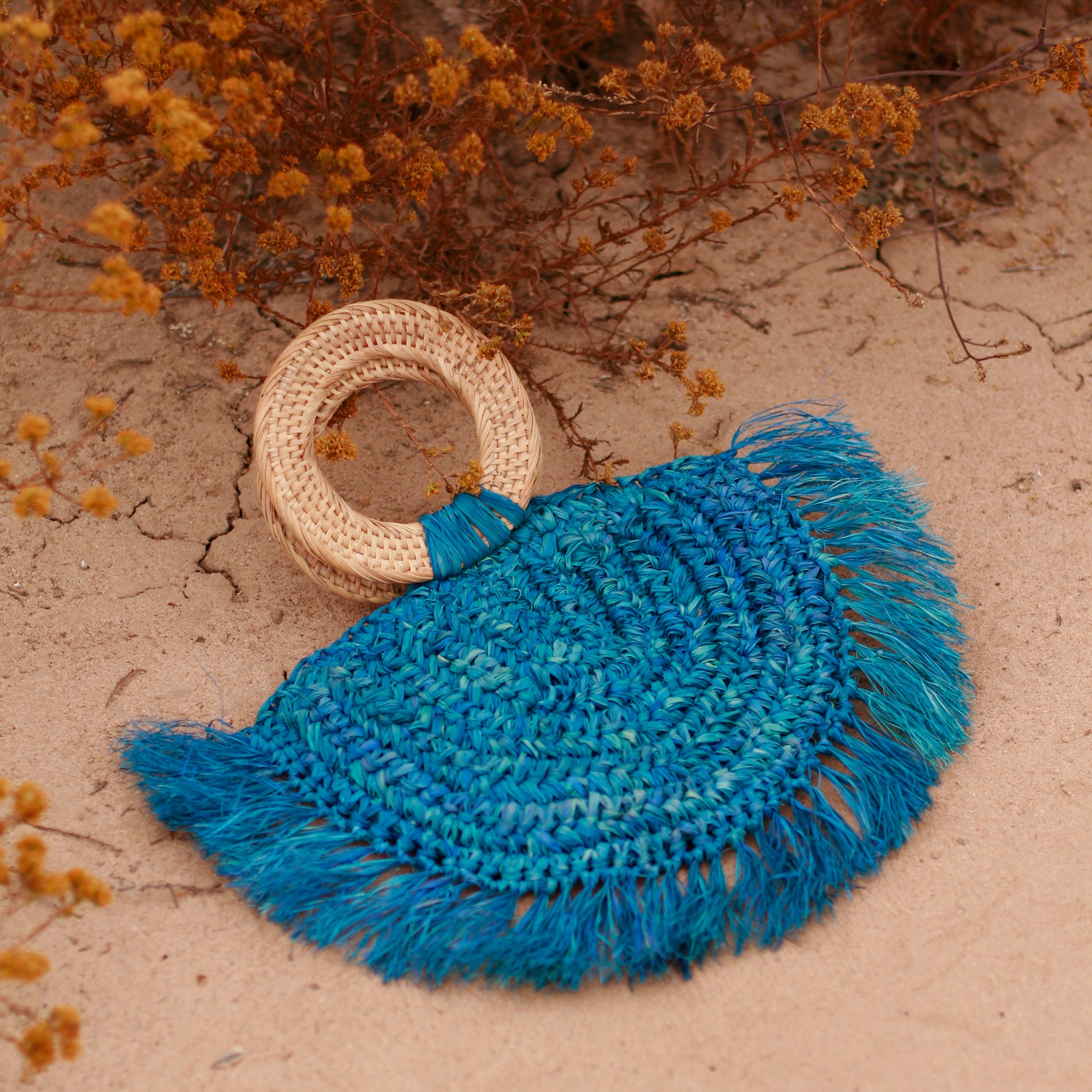 Warrior Raffia Straw Bag in Blue, handcrafted with natural Raffia straw, featuring fringes and a stylish rattan handle.