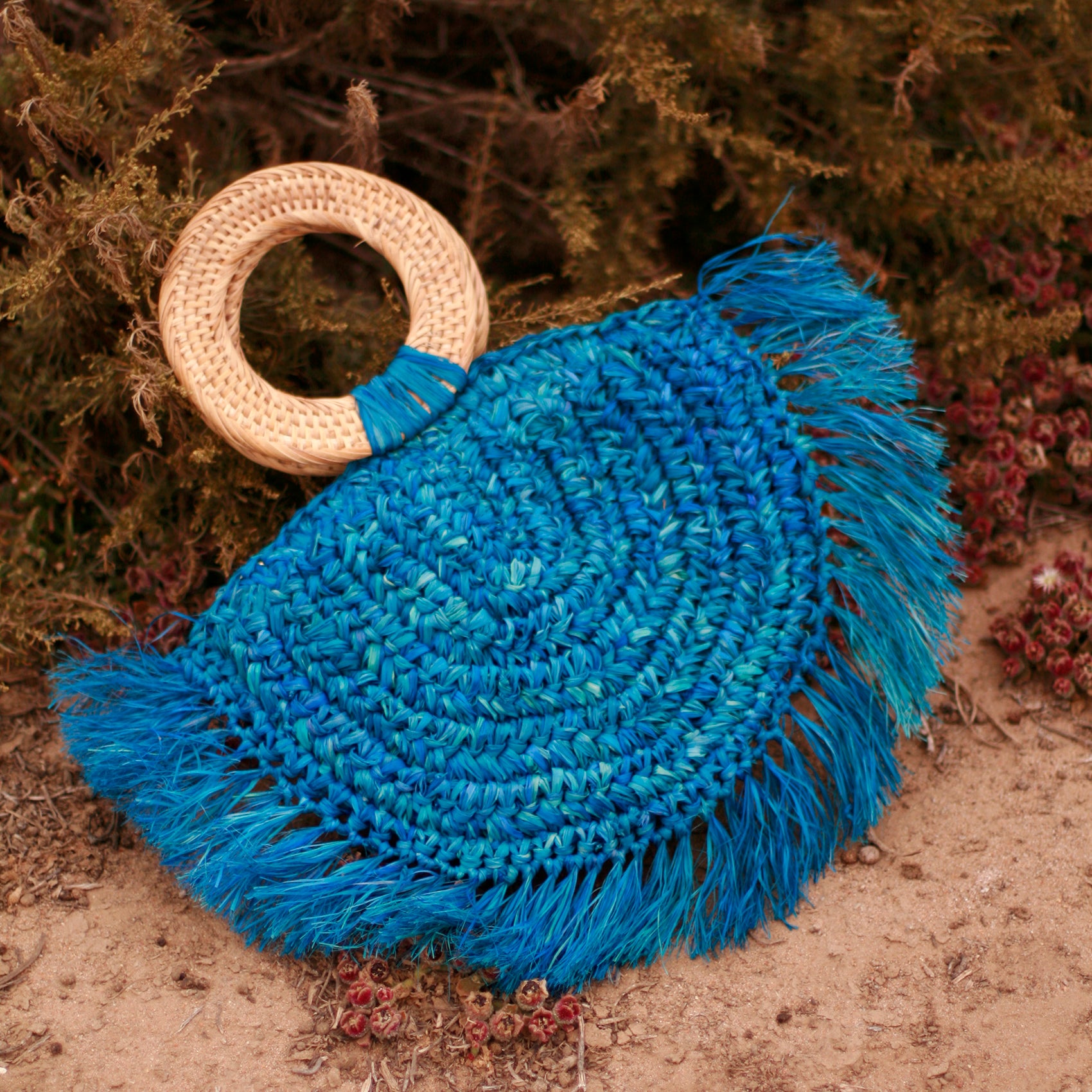 Warrior Raffia Straw Bag in Blue, handcrafted with natural Raffia straw, featuring fringes and a stylish rattan handle.