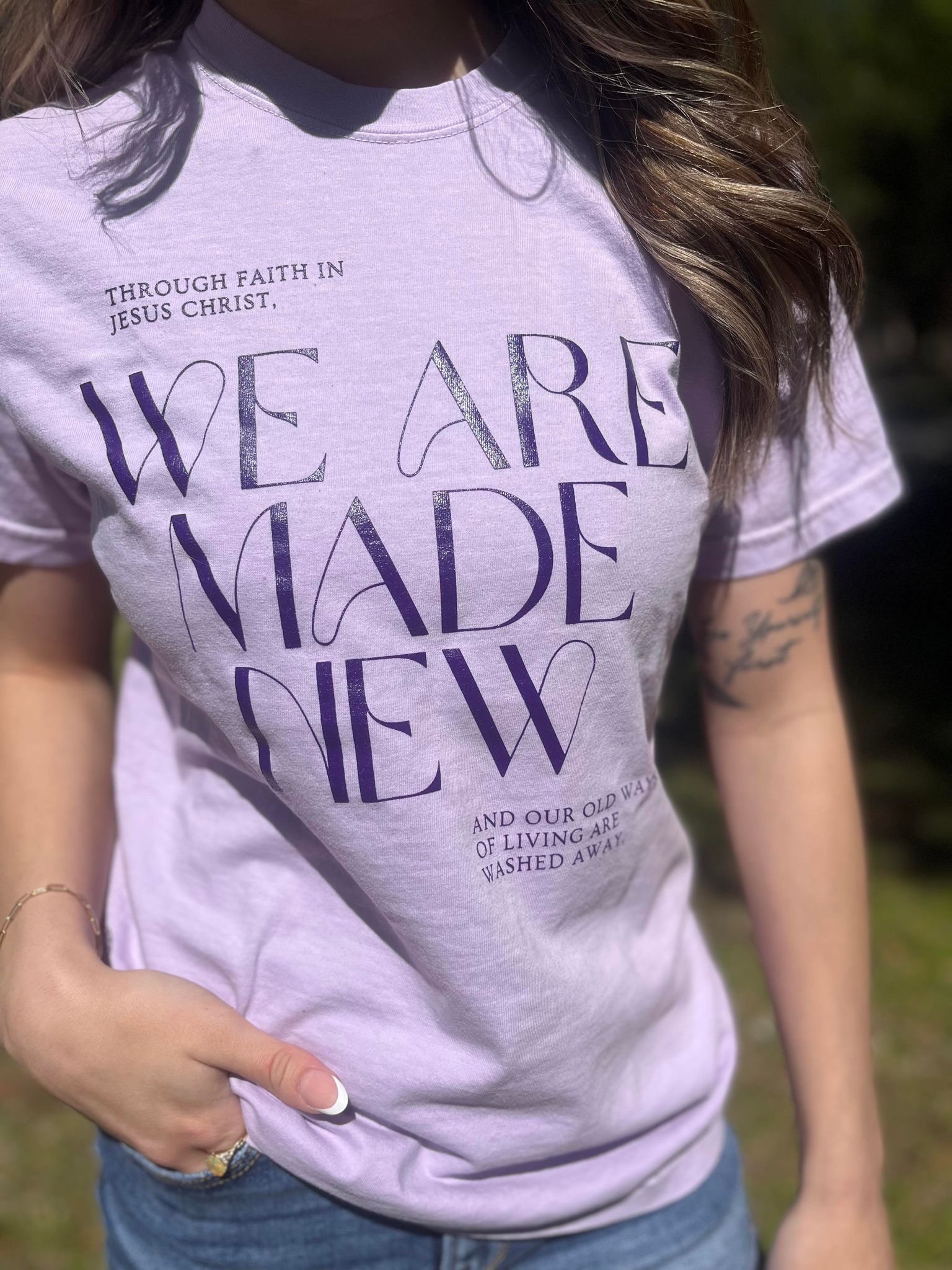 A stylish monochrome purple tee with the text 'We Are Made New' printed on it, showcasing a comfortable fit.