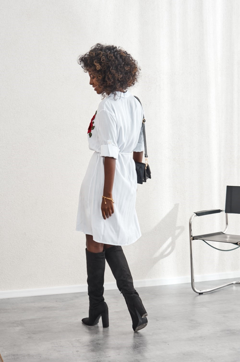 A stylish white shirt dress featuring beautiful embroidered flowers, buttoned from collar to waist with rolled-up sleeves and a tied belt.