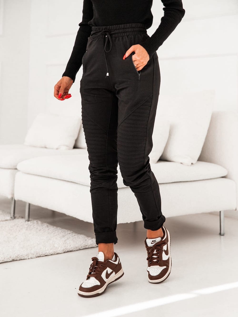 Women's black sweatpants with decorative stitching and zippered pockets, featuring an elastic waist and cuffs.