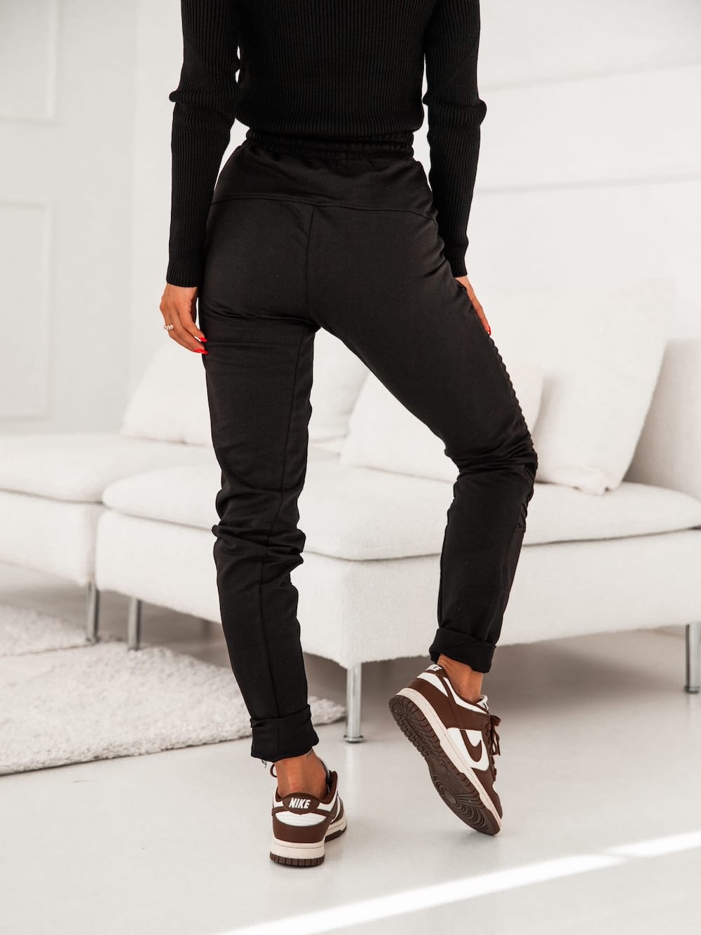 Women's black sweatpants with decorative stitching and zippered pockets, featuring an elastic waist and cuffs.