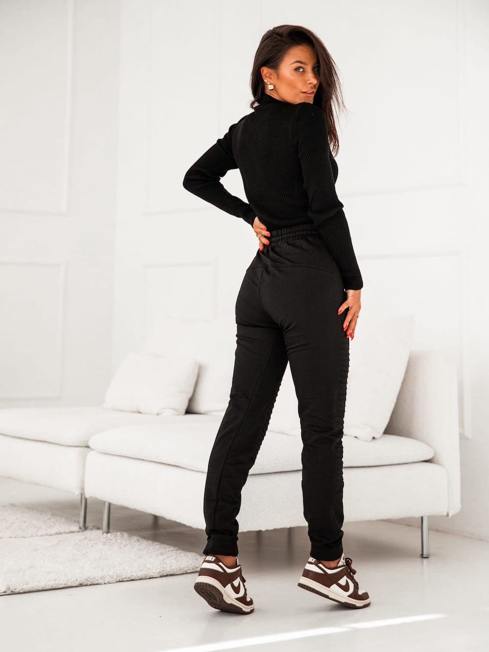 Women's black sweatpants with decorative stitching and zippered pockets, featuring an elastic waist and cuffs.