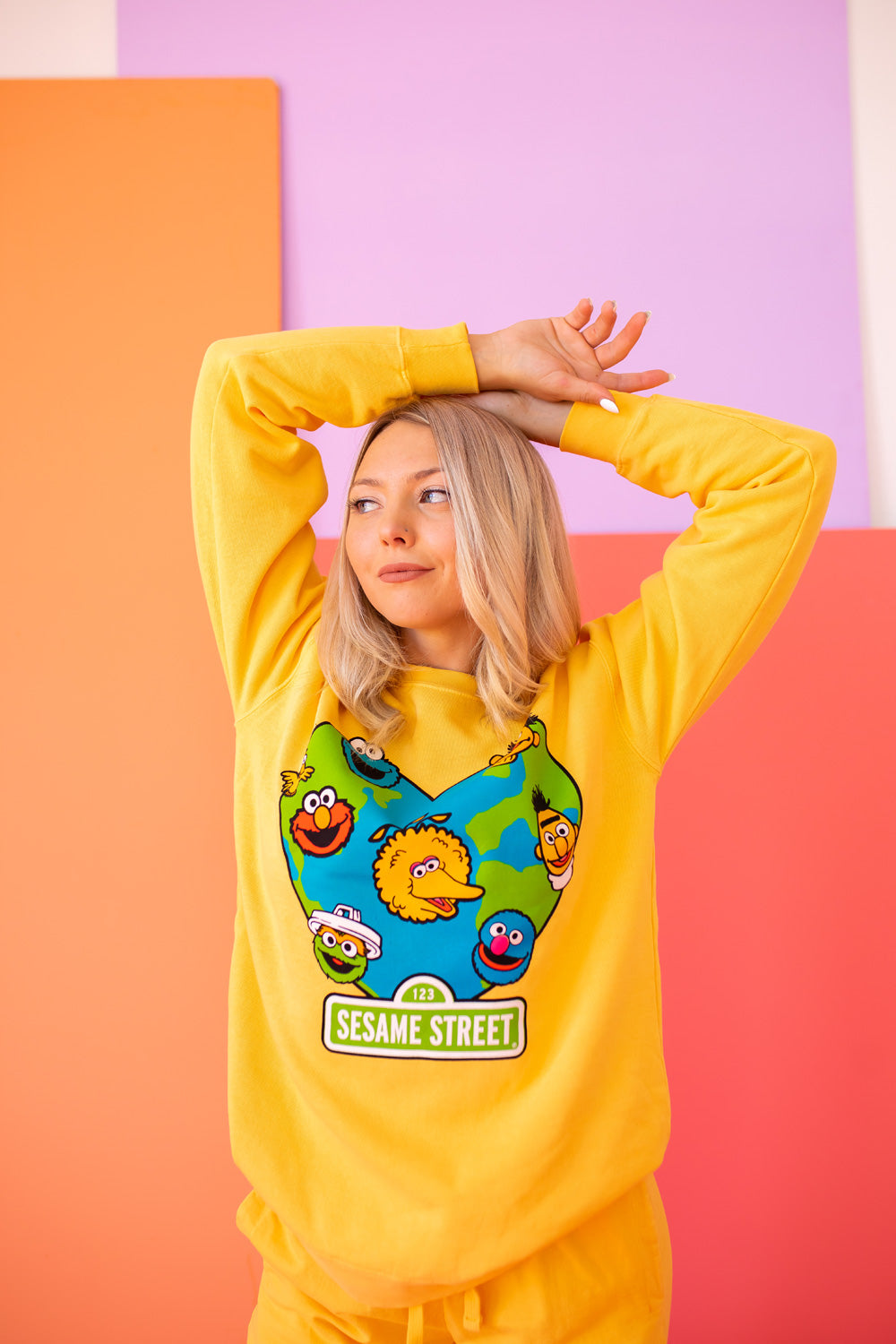 A vibrant yellow sweatshirt featuring iconic Sesame Street characters, made from 100% upcycled cotton, perfect for casual wear.