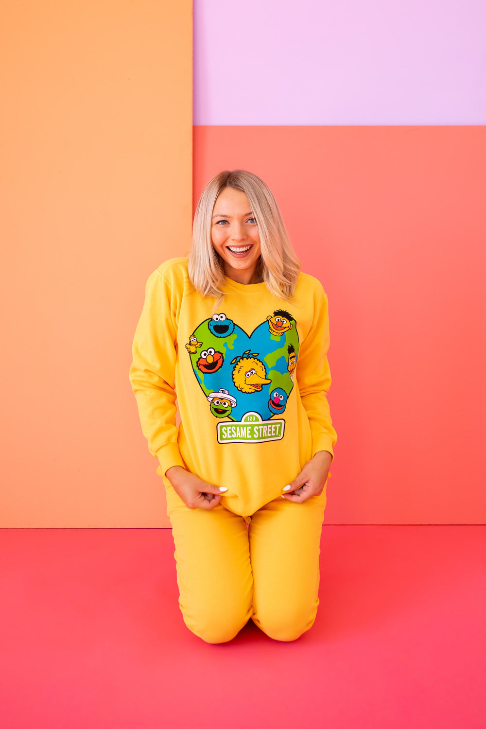 A vibrant yellow sweatshirt featuring iconic Sesame Street characters, made from 100% upcycled cotton, perfect for casual wear.