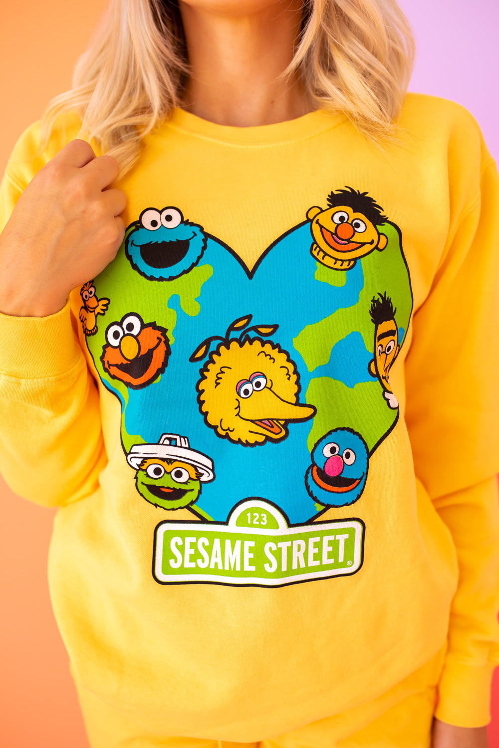 A vibrant yellow sweatshirt featuring iconic Sesame Street characters, made from 100% upcycled cotton, perfect for casual wear.