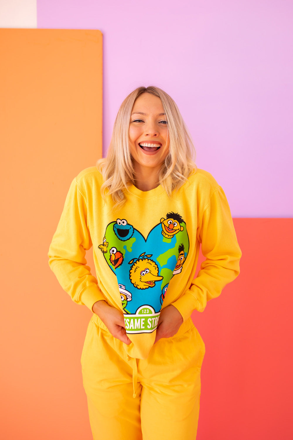 A vibrant yellow sweatshirt featuring iconic Sesame Street characters, made from 100% upcycled cotton, perfect for casual wear.